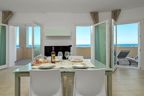 Un coin repas avec une table dressée pour deux personnes, un téléviseur et une vue sur la mer.