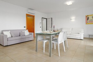 A modern living room with a grey sofa, a dining table with chairs, a white sofa, and a wooden door.