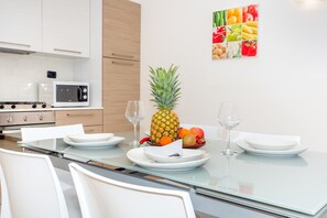 Une cuisine moderne avec des meubles blancs, un four à micro-ondes et une table à manger pour deux personnes, avec de l’assiette et des verres blancs.