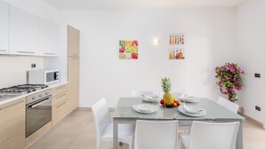A modern kitchen with white cabinets, a microwave, and a dining table set for four with white chairs. - Bright Apartment "Villa Marconi 4" with Sea view, Private Terrace & Garden (Golfo Aranci)
