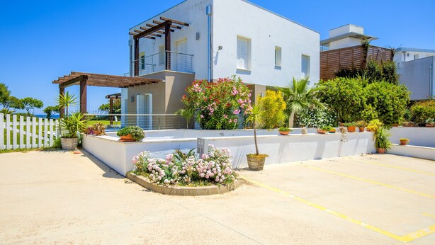 A modern two-story house with a balcony, a white exterior, and a garden with various plants and flowers. - Bright Apartment "Villa Marconi 4" with Sea view, Private Terrace & Garden (Golfo Aranci)