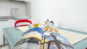 A kitchen with white cabinets, a red chair, a glass table, and a magazine with a beach scene. - Spacious Apartment "Villa Marconi 6" with Sea View, Private Terrace & Garden (Golfo Aranci)