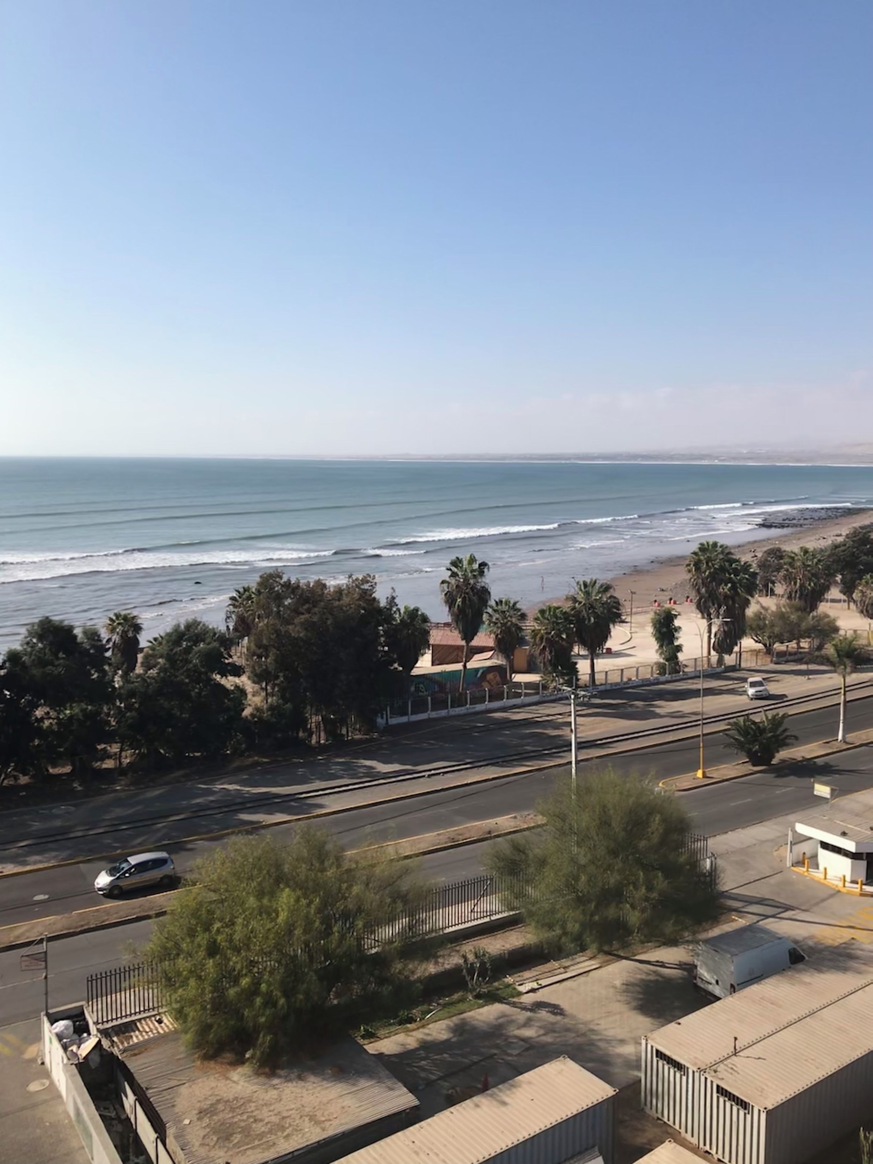 Eine Küstenstraße mit Strand und Palmen in der Ferne.