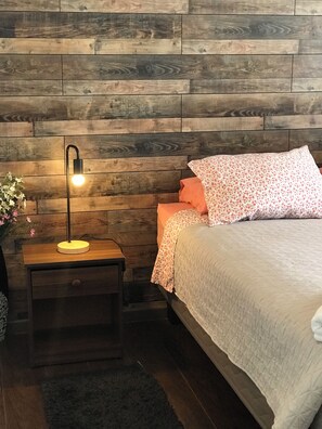A bedroom with a wooden headboard, a bedside table with a lamp, a bed with floral bedding, and a dark rug.