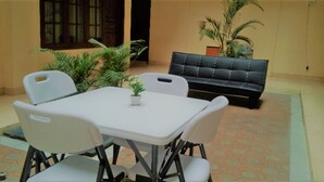 Een eethoek met een witte tafel, vier stoelen, een zwarte bank en potplanten.