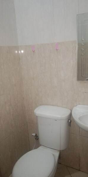 A bathroom with a toilet and sink, beige tiles, and a mirror above the sink. - Residence Duksina 2 by SHM (Depok)