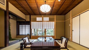 A tatami mat room with a low table and chairs, wooden beams on the ceiling, and sliding doors.