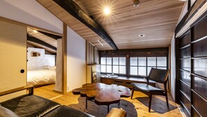 A modern interior with a wooden ceiling, a bed, a leather sofa, a wooden coffee table, and a view through a large window.