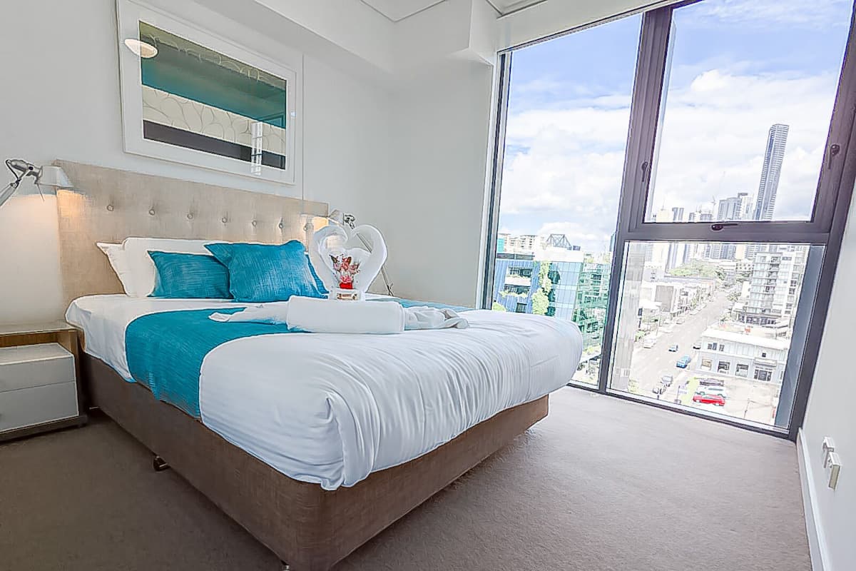 A modern bedroom with a large bed, a city view, and a framed artwork above the bed.