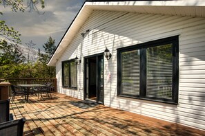 A house with a deck, a dining area with chairs, and a door.