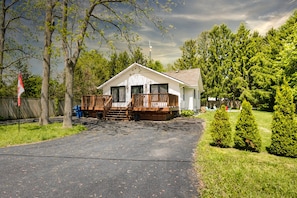 A single-story mobile home with a front deck, surrounded by trees and a grassy yard.