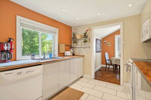 Una cocina moderna con armarios blancos, lavavajillas, cafetera y ventana con vistas al verdor.