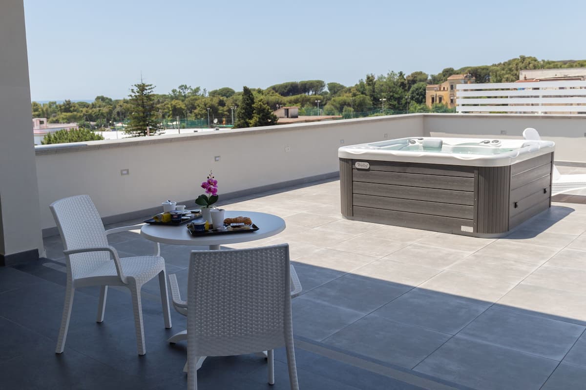 Terraço no telhado com hidromassagem, duas cadeiras brancas e uma mesa com um vaso de flores.
