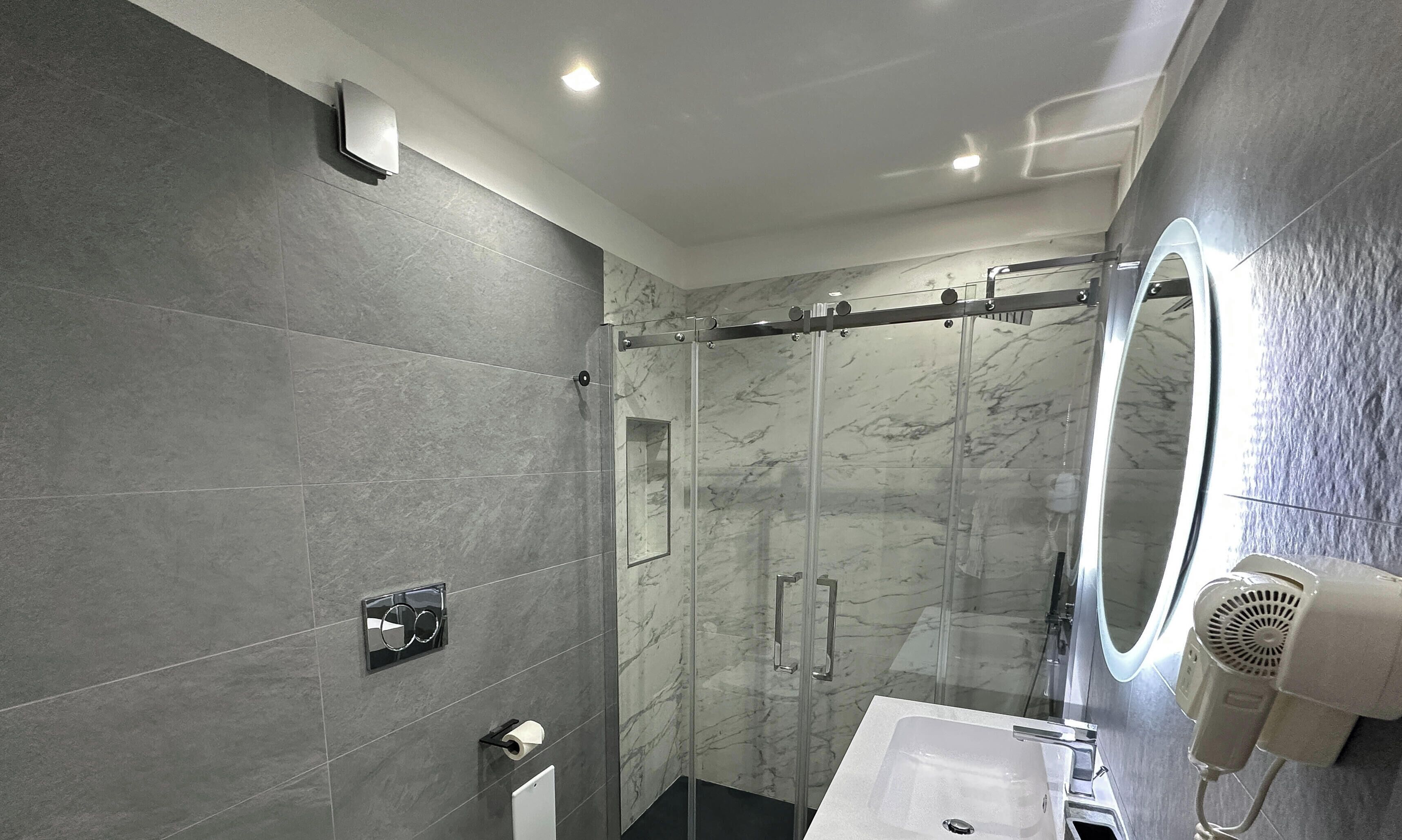 Een moderne badkamer met een douchecabine van glas, een wastafelmeubel en een haardroger bevestigd aan de muur.