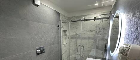 Een moderne badkamer met een douchecabine van glas, een wastafelmeubel en een haardroger bevestigd aan de muur.