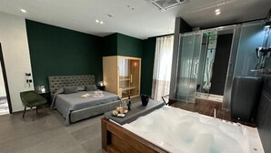 Un dormitorio moderno con una cama grande, un sofá cama independiente, un vestidor, cabina de ducha con mampara de vidrio y un baño separado con bañera.