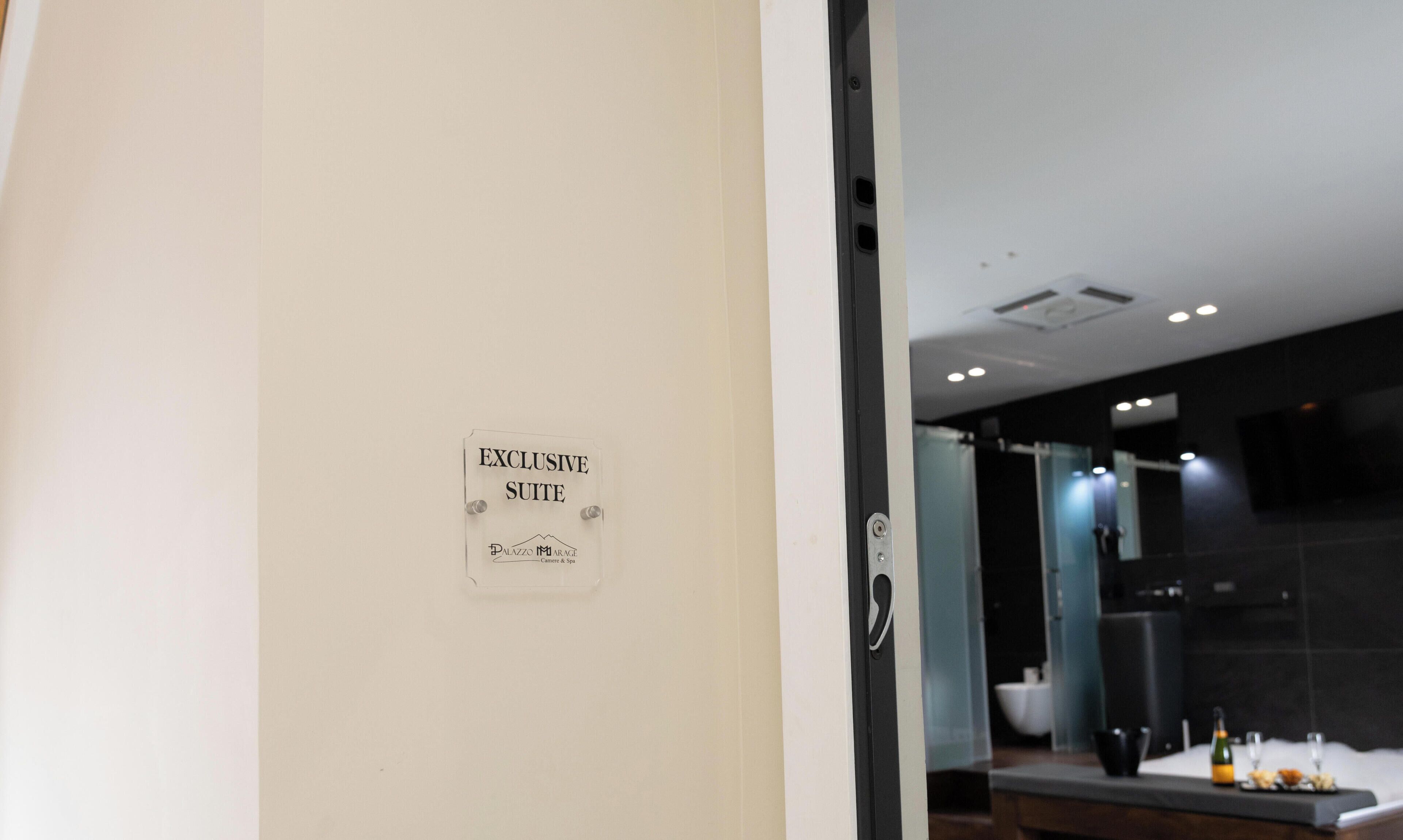 Une pancarte indiquant qu’il s’agit d’une suite de luxe, une salle de bain moderne avec une douche en verre et une table de petit-déjeuner avec une bouteille et des verres.
