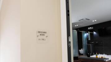 A sign indicating an exclusive suite, a modern bathroom with a glass shower, and a breakfast setup with a bottle and glasses.