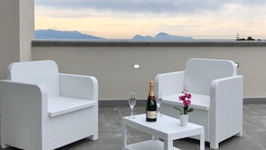 Un balcón con dos sillas blancas de mimbre, una mesita con una botella de champán y una copa, y una orquídea en maceta.