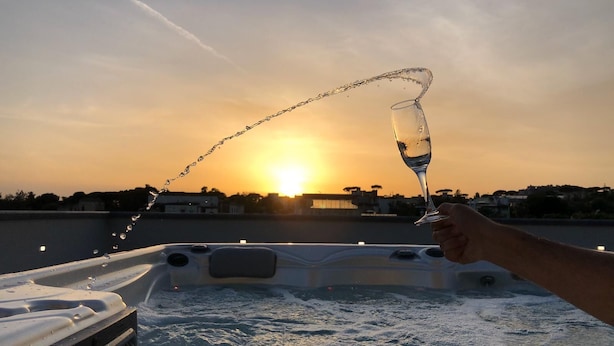 Una persona vertiendo agua de un vaso en una bañera de hidromasaje al atardecer.
