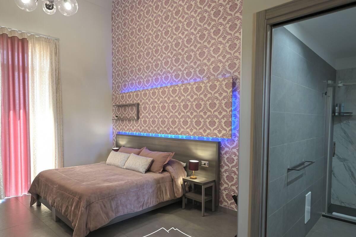 Quarto com cama, mesa de cabeceira e chuveiro.
