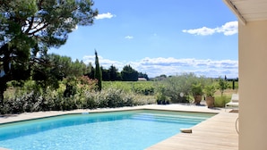 A swimming pool with a wooden deck, surrounded by lush greenery and a clear blue sky. - Le Clos Vitis - Chambres d'hôtes et gite (Violes)