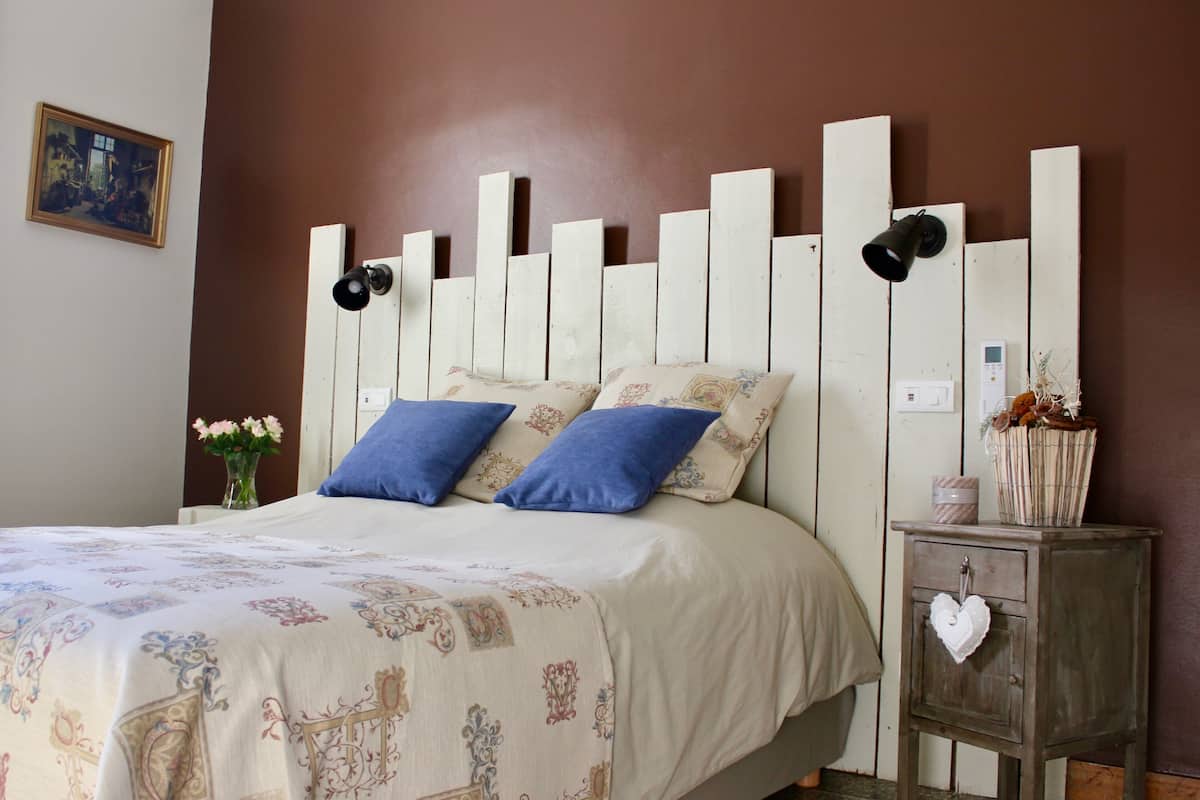 A bedroom with a bed, two pillows, a bedside table with a vase, and a wall-mounted light.