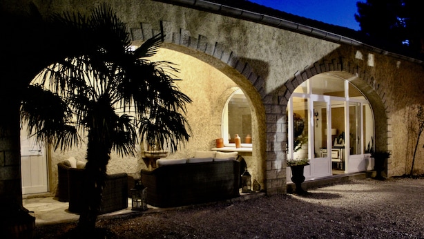 A stone building with arched windows and a patio area with furniture and a palm tree. - Le Clos Vitis - Chambres d'hôtes et gite (Violes)