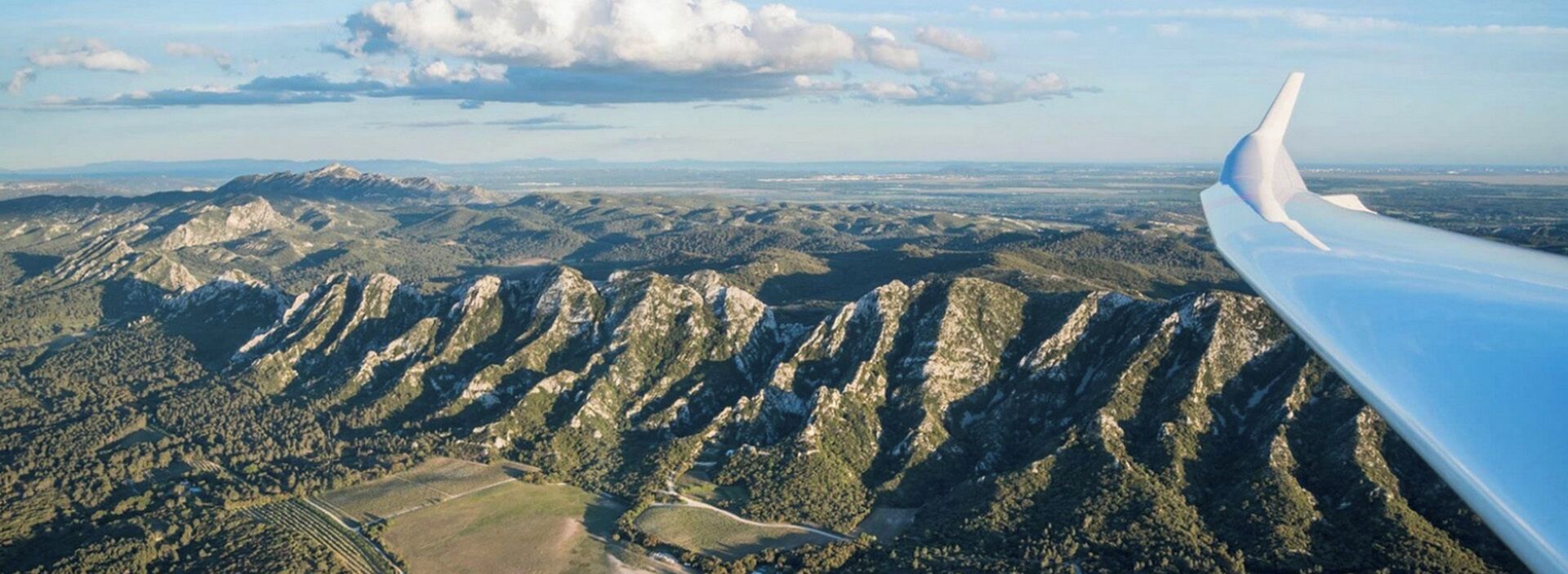 Flügel eines Flugzeugs mit einer Berglandschaft im Hintergrund.