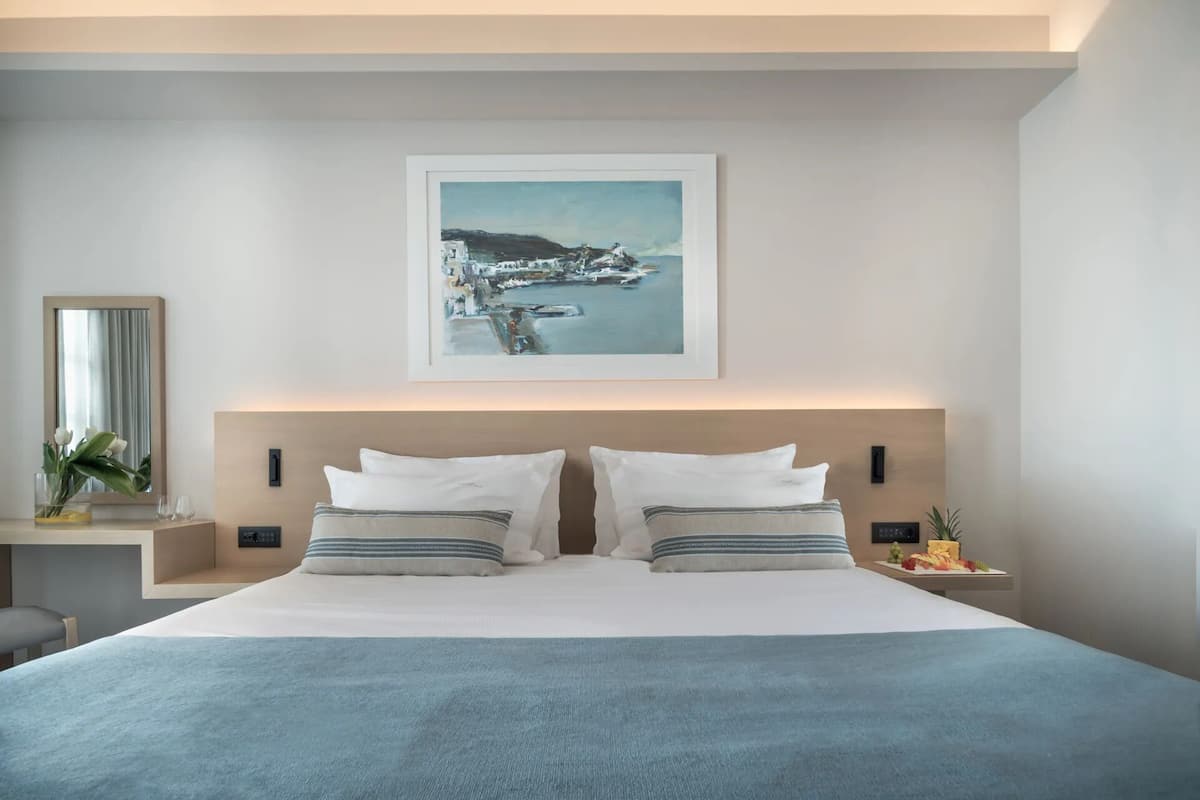 A modern bedroom with a large bed, two bedside tables, a framed artwork above the bed, and a nightstand with a fruit plate.