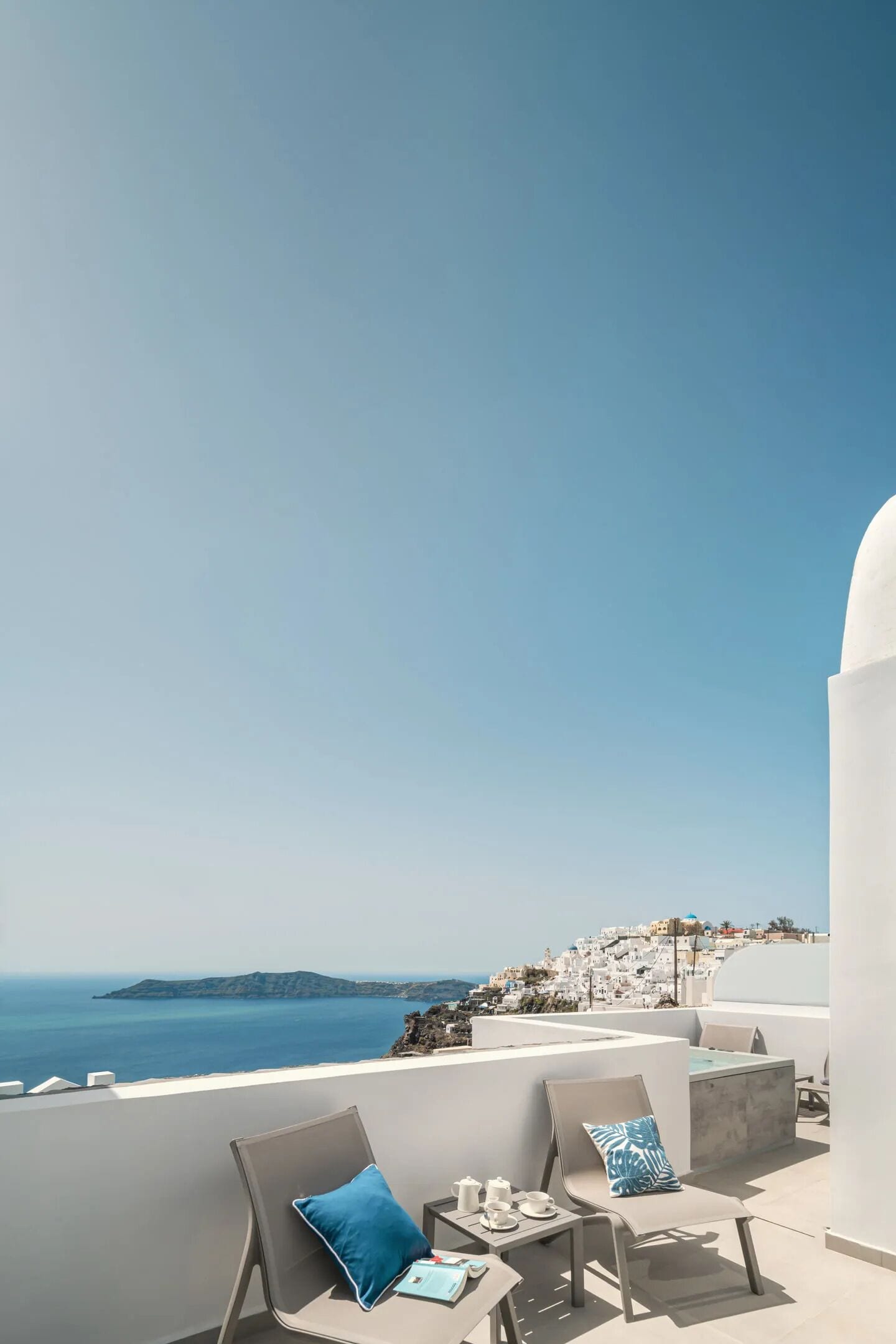Terraza con dos sillas y una mesa, con vistas a un pueblo costero y al mar.