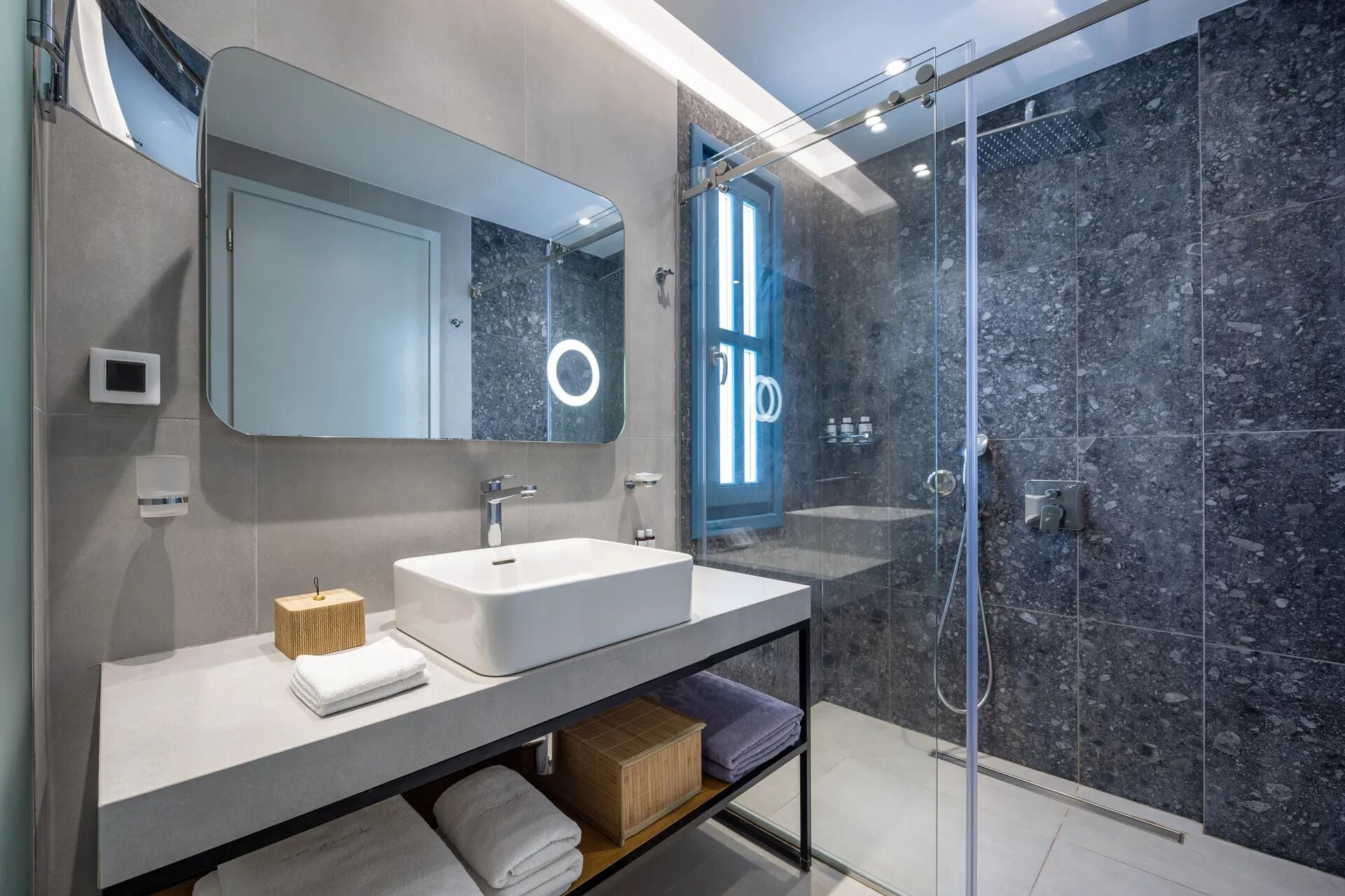 A modern bathroom with a large mirror, two sinks, a glass shower enclosure, and a towel rack.