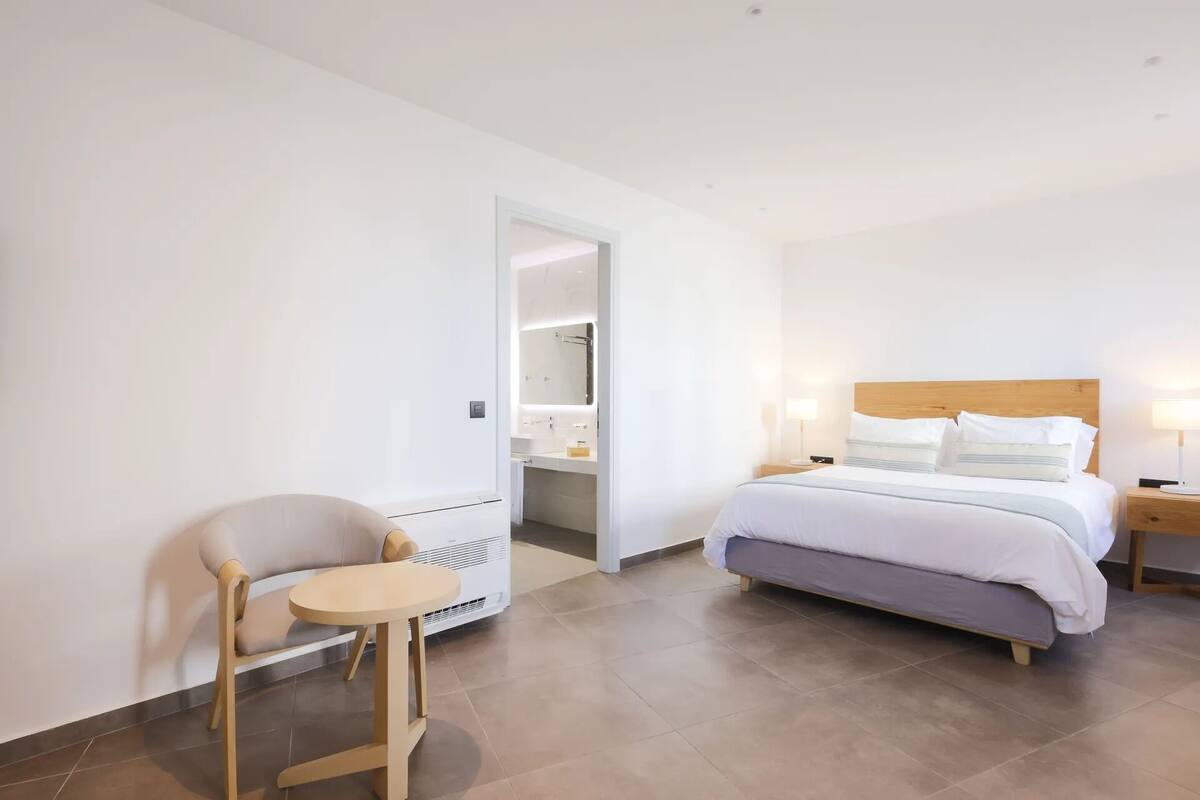 A hotel room with a bed, bedside table, chair, and a bathroom visible through an open door.