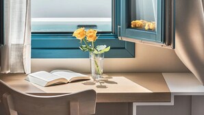 A room with a large window, a desk with an open book, and a vase with flowers. - Aeifos Boutique Hotel (Santorini)