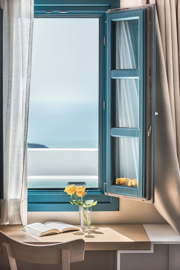 Una habitación con un ventanal grande, un escritorio con un libro abierto y un jarrón con flores.