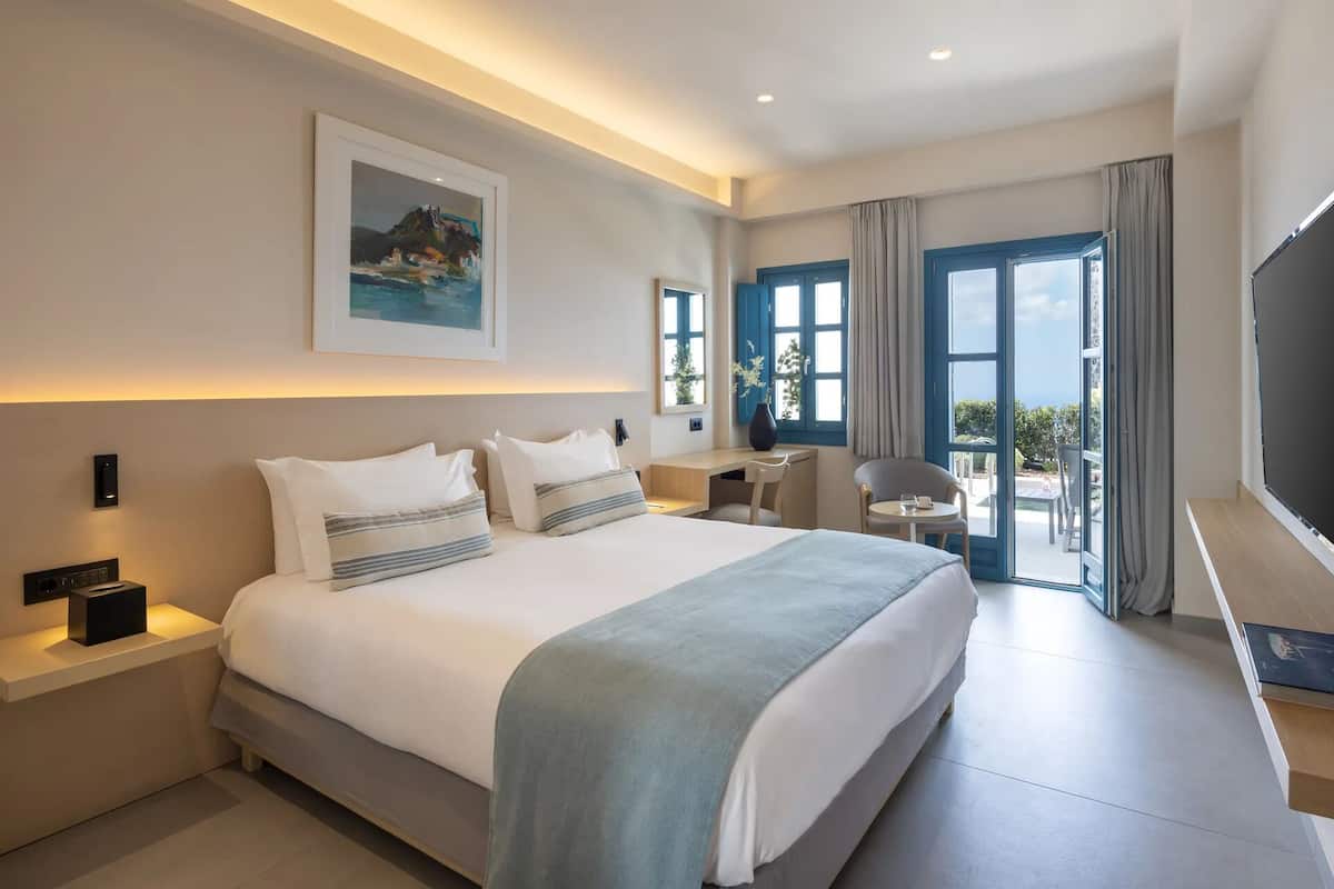 A modern hotel room with a large bed, a desk, a chair, and a TV.