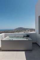 Un jacuzzi moderno al aire libre en un balcón con vistas despejadas a un pueblo costero y montañas al fondo.