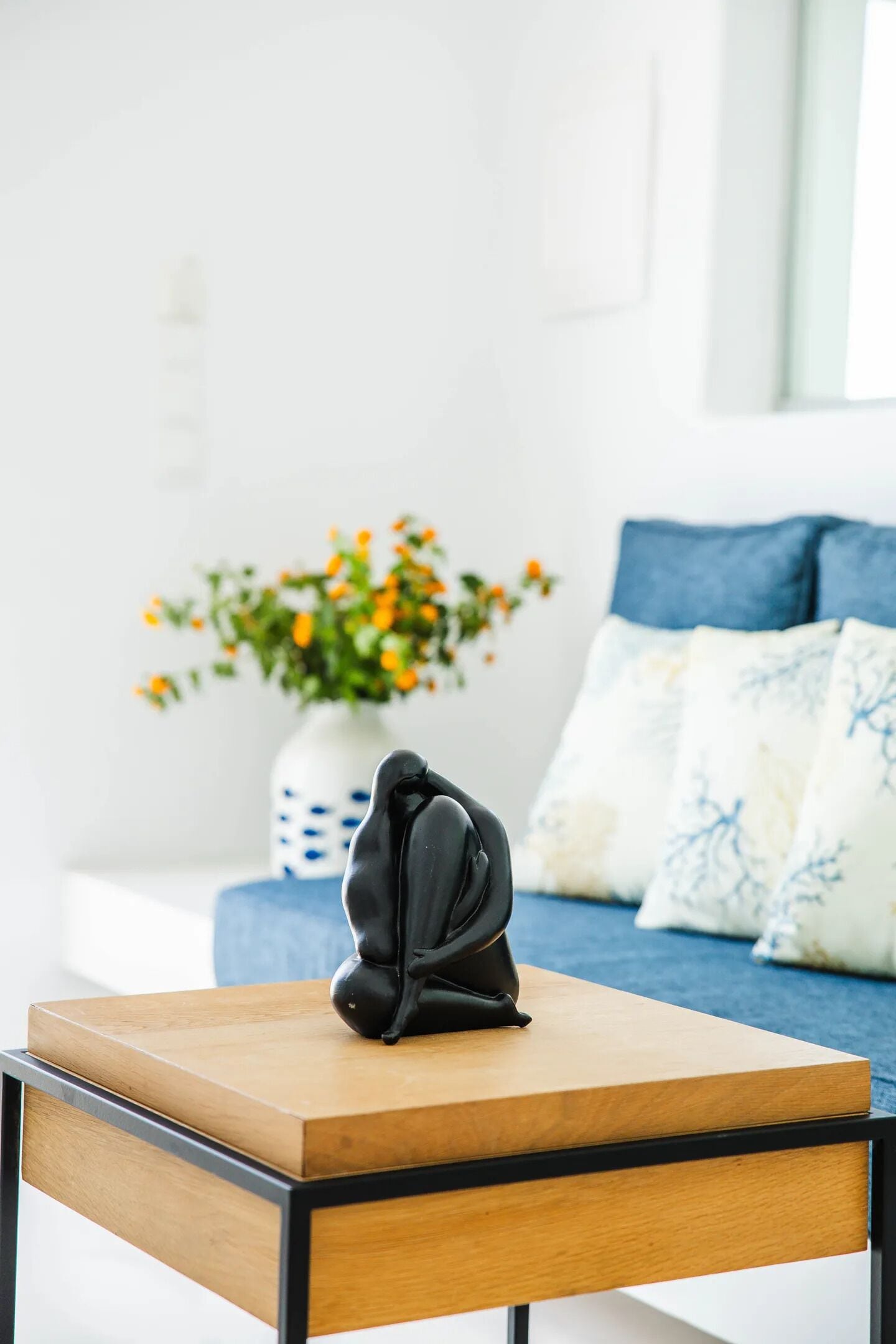 A modern living room with a wooden coffee table, a black sculpture, and a vase with orange flowers.