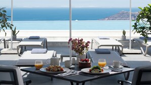 Eine Terrasse mit weißen Sonnenschirmen, gedecktem Frühstückstisch und Meerblick.
