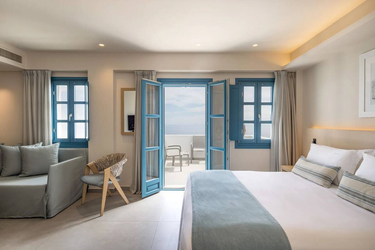 A hotel room with a large bed, a sofa, a chair, and a balcony with a view.