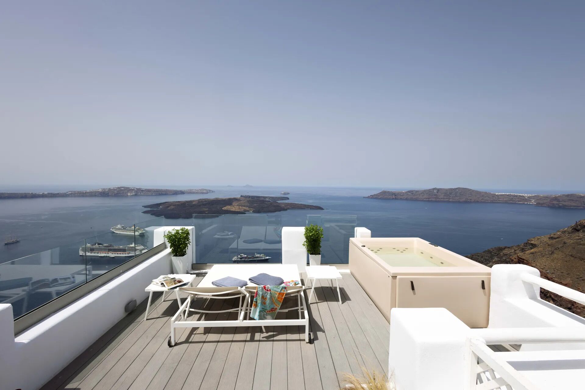 A terrace with white furniture, a glass balustrade, and a view of the sea and islands.