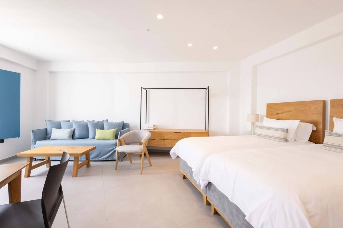 A modern hotel room with a bed, a sofa, a desk, and a chair.