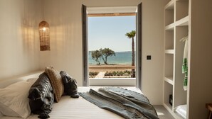A bedroom with a bed, a view of the beach, and a shelf with towels. - Seesoo Paros Beachfront Luxury Hideaway (Paros)