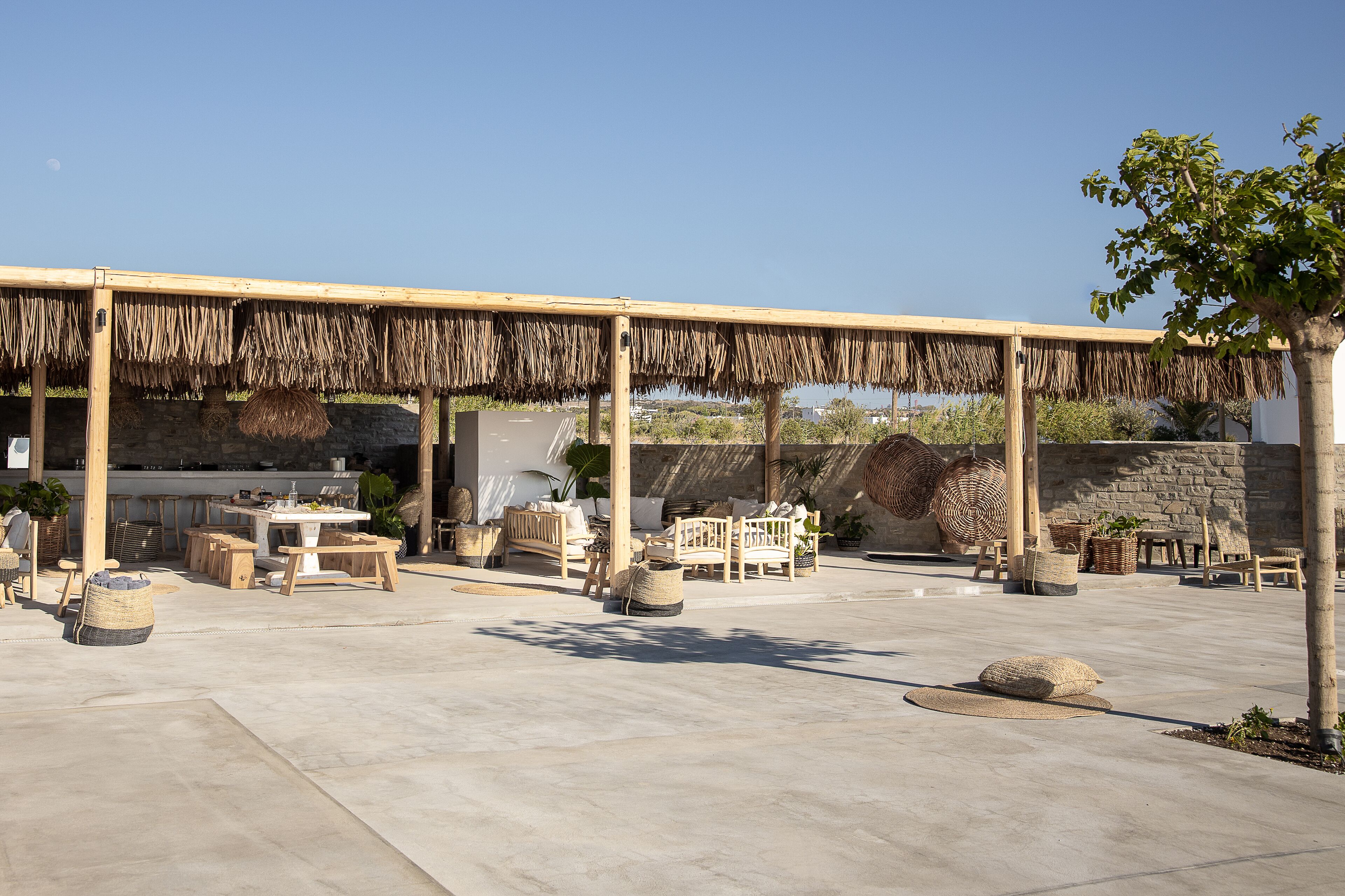 An outdoor patio area with wooden furniture, woven baskets, and a stone wall backdrop.