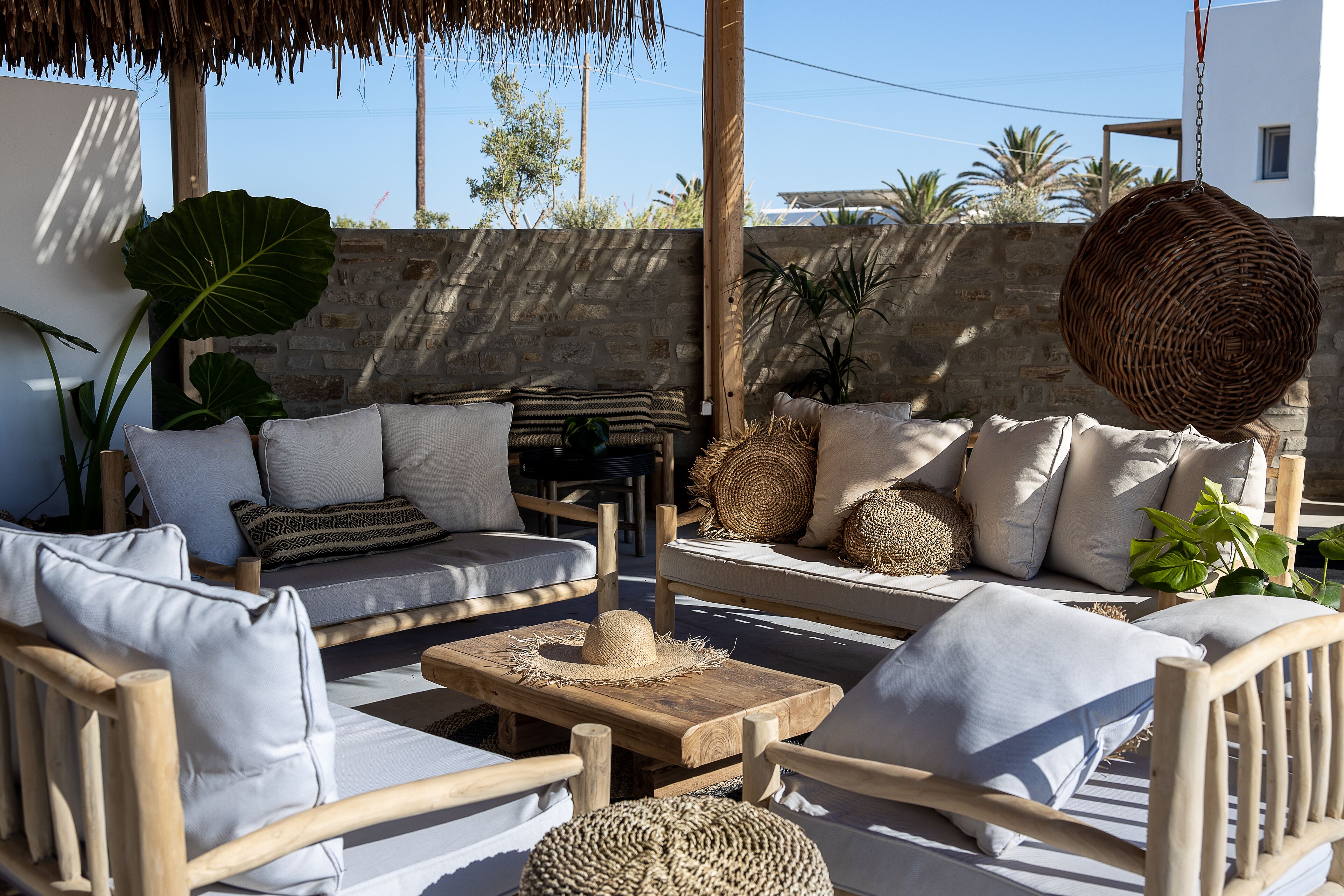 A sunlit outdoor seating area with wooden furniture, cushions, and woven baskets.
