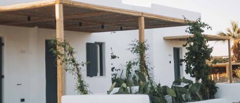 A modern white building with a wooden pergola, outdoor seating, and potted plants.