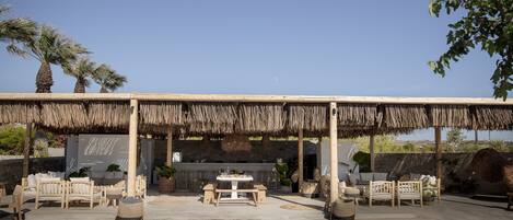 An outdoor seating area with a thatched roof, wooden furniture, and potted plants.