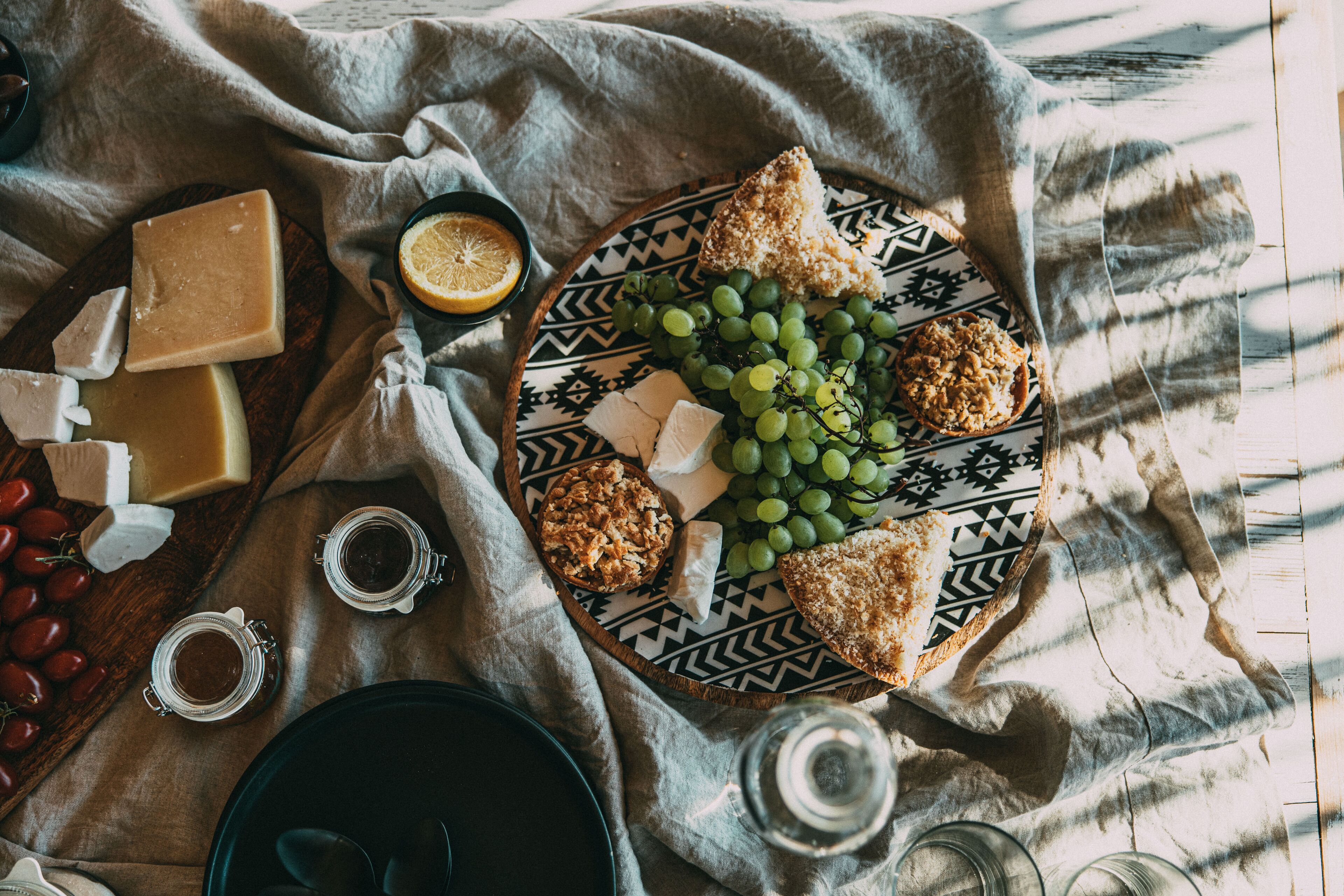 Una tabla de quesos con diferentes tipos de queso, uvas y galletas sobre un plato estampado, junto a un tazón de cerezas y un vaso de jugo.