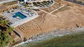 An aerial view of a modern resort with a swimming pool, sun loungers, and a landscaped area with palm trees. - Seesoo Paros Beachfront Luxury Hideaway (Paros)