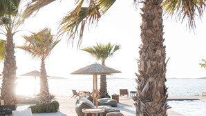 A beachside lounge with palm trees, lounge chairs, and a pool. - Seesoo Paros Beachfront Luxury Hideaway (Paros)